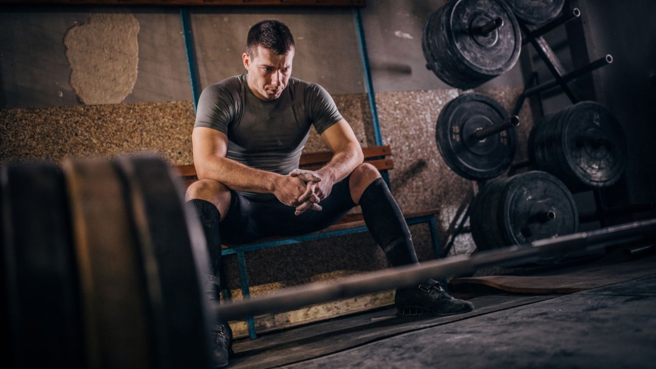 homem sentado em frente a uma barra de peso sem vontade de treinar