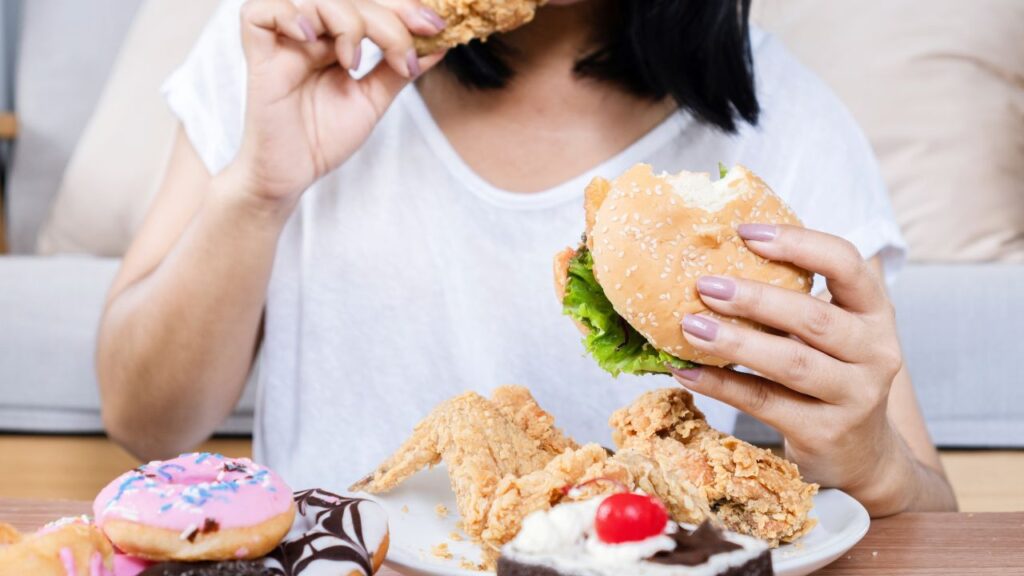 mulher comendo várias comidas não saudáveis 