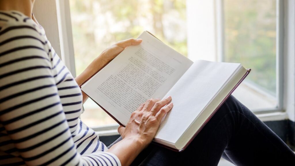 mulher lendo livro próximo a uma janela