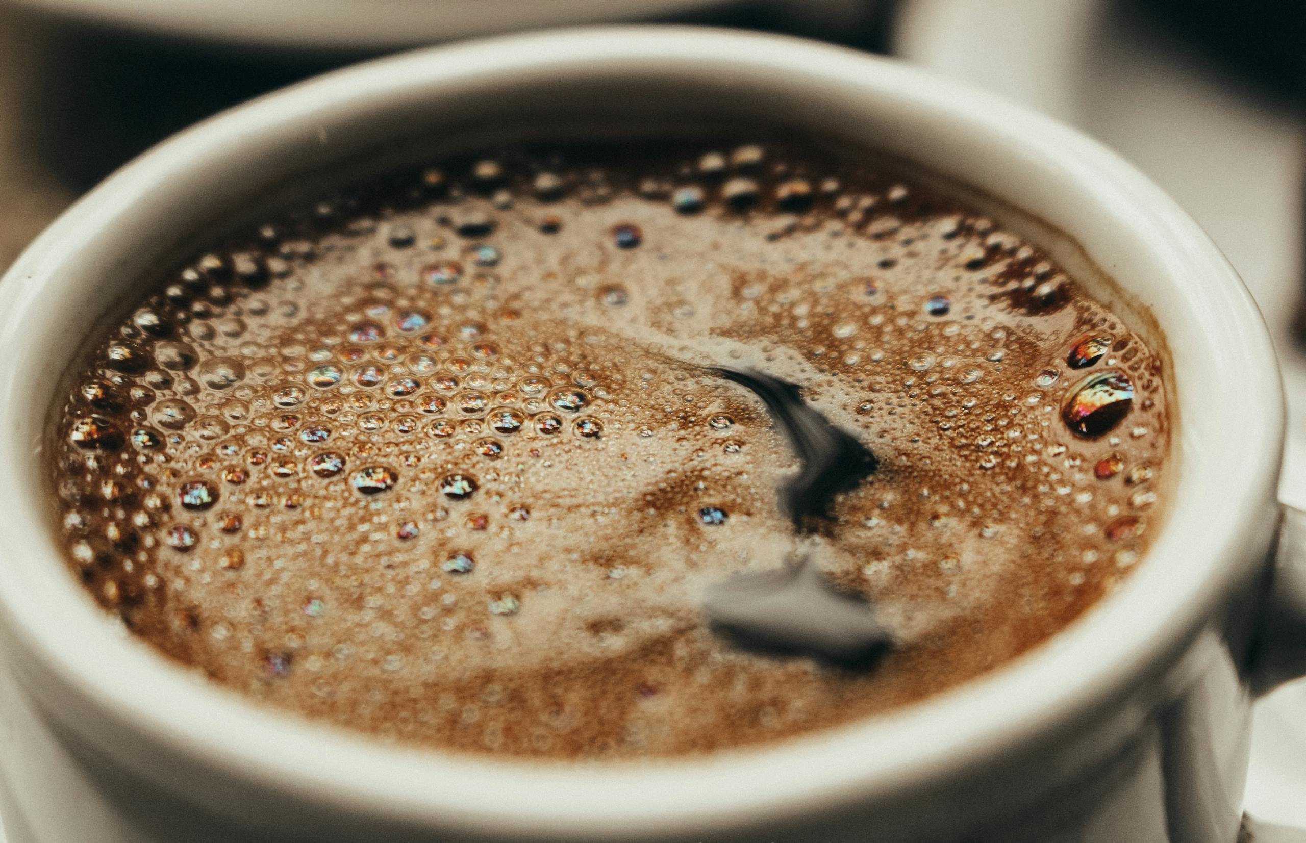 A close-up photo showcasing freshly brewed coffee in a white cup with visible bubbles.